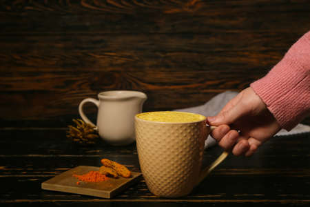 Female hand with cup of tasty turmeric latte on wooden backgroundの写真素材