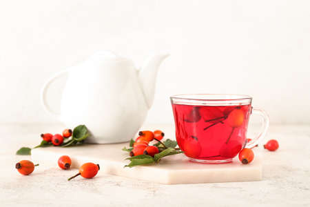 Glass cup of tasty rose hip tea and berries on light backgroundの写真素材