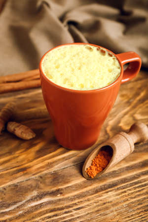 Cup of tasty latte and scoop with turmeric powder on wooden backgroundの写真素材