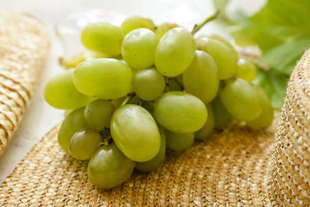 Ripe grapes and straw hat on table, closeup