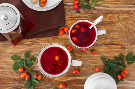 Cups of tasty rose hip tea and berries on wooden background