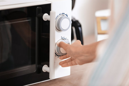 Young woman adjusting microwave oven in kitchen, closeupの写真素材