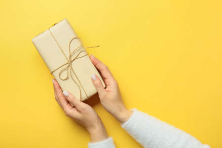 Female hands with gift box on yellow background, closeupの写真素材