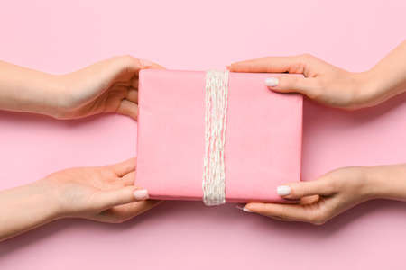 Female hands with gift box on pink background, closeupの写真素材