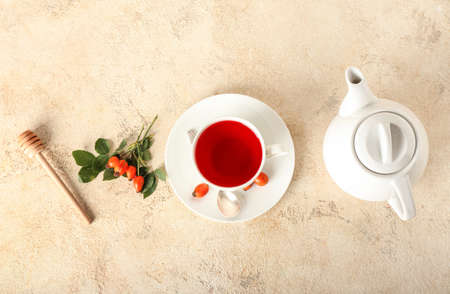 Cup of tasty rose hip tea, pot, berries and dipper on light backgroundの写真素材