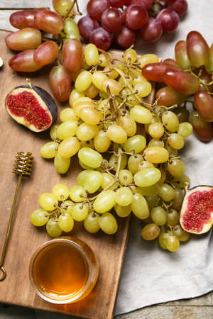 Sweet ripe grapes, fig and honey on wooden background, closeup