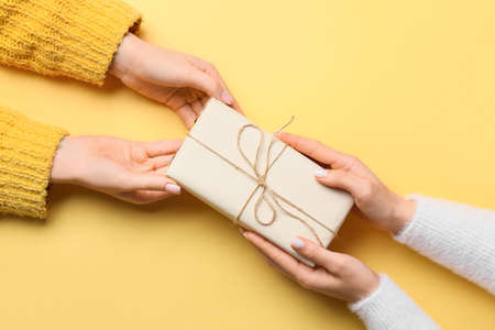 Female hands with gift box on yellow background, closeupの写真素材