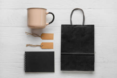Composition with cup, blank paper bag, tags and notebook on light wooden backgroundの写真素材