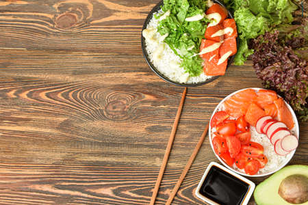 Tasty poke bowls with salmon, vegetables and sauce on wooden backgroundの写真素材