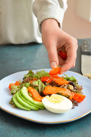 Woman preparing fresh salad with salmon and vegetables at table, closeup