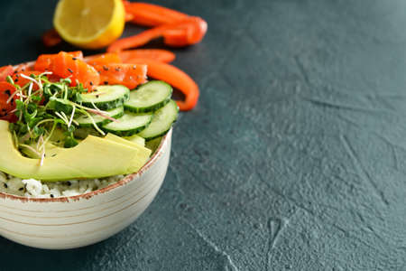 Tasty poke bowl with salmon and vegetables on dark background