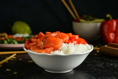 Tasty poke bowl with salmon and vegetables on dark table