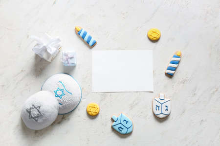 Tasty cookies for Hanukkah celebration and blank paper sheet and Jewish hats on white background