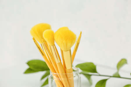 Glass with set of makeup brushes on table, closeup