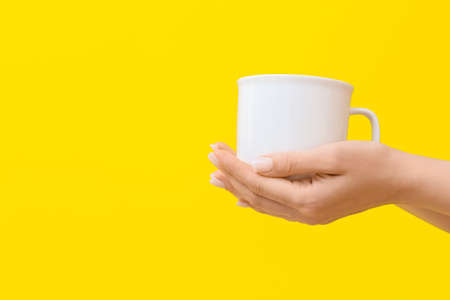 Woman holding cup on yellow background, closeupの写真素材