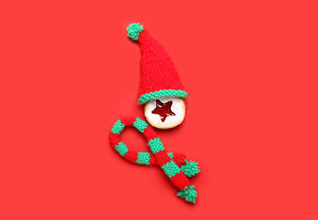 Tasty Linzer cookie with knitted hat and scarf on color background