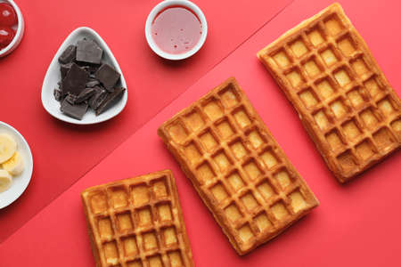 Delicious Belgian waffles with chocolate, jam and banana on color background
