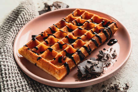 Plate with delicious Belgian waffle and chocolate syrup on light background, closeup