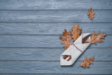 Napkin, cutlery and autumn leaves on color wooden backgroundの写真素材