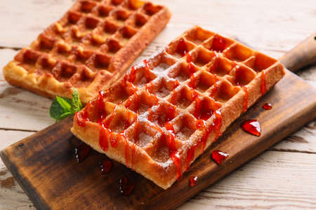Board with delicious Belgian waffles and jam on light wooden background, closeup