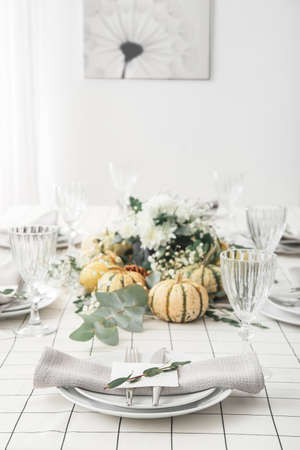 Stylish table setting with card and autumn decor in light roomの写真素材