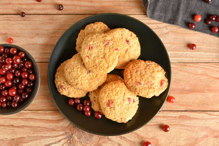 Plate with fresh cranberry cookies and berries on wooden backgroundの写真素材