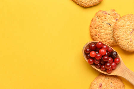 Tasty cranberry cookies and spoon with berries on yellow background, closeupの写真素材