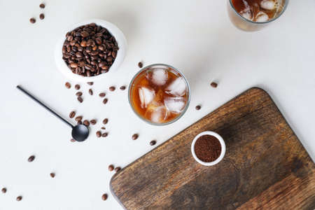 Glass of cold brew with milk and scattered coffee beans on white tableの写真素材