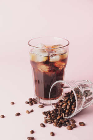 Glasses with cold brew and coffee beans on pink background
