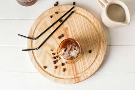 Wooden board with glass of cold brew coffee, milk and straws on white tableの写真素材