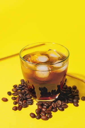 Glass with cold brew and coffee beans on yellow background, closeup