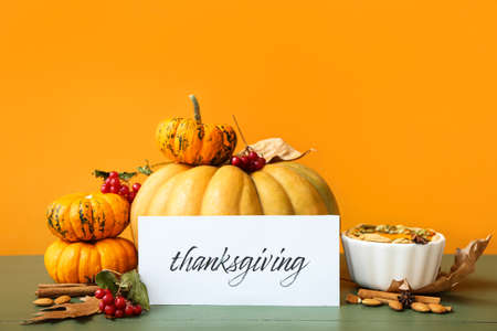 Different pumpkins, pie and text THANKSGIVING on wooden table against color wall