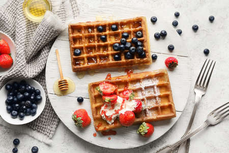 Wooden board of tasty Belgian Waffles with berries on light background