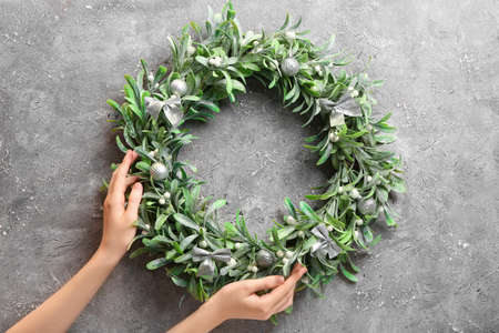 Female hands with beautiful mistletoe wreath on grunge backgroundの写真素材