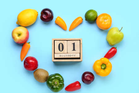 Heart shaped frame made of fresh products and cube calendar with date NOVEMBER 1 on blue background....