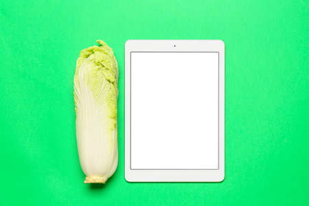 Chinese cabbage and tablet computer on green background. World Vegan Day concept