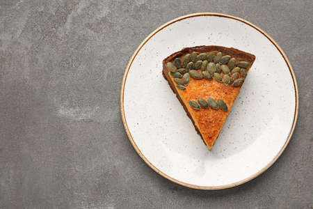 Plate with piece of delicious pumpkin pie on gray background