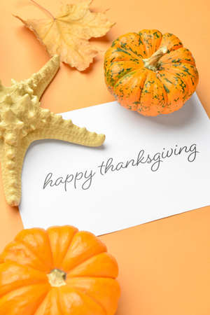 Starfish, pumpkins, autumn leaves and paper card with text THANKSGIVING on color background, closeupの写真素材