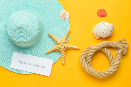 Beach hat, starfish, seashells, rope and paper card with text HAPPY THANKSGIVING on color backgroundの写真素材