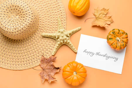 Beach hat, starfish, pumpkins, autumn leaves and paper card with text THANKSGIVING on color backgroundの写真素材