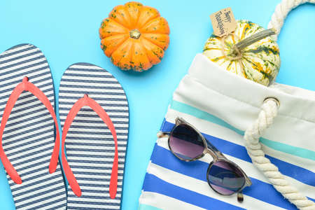 Flip flops, beach bag, sunglasses, pumpkins and paper card with text HAPPY THANKSGIVING on color background, closeupの写真素材