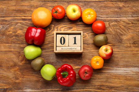 Frame made of fresh vegetables, fruits and wooden cube calendar with date NOVEMBER 1 on wooden background. World Vegan Day conceptの写真素材