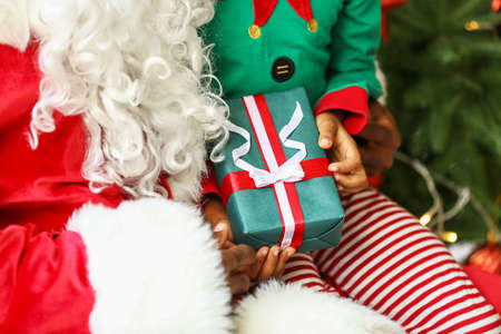 Santa Claus giving present to little African-American boy at home, closeup