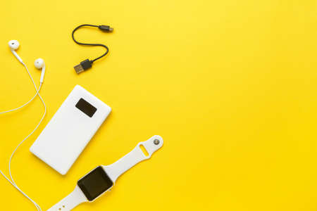 Modern power bank, smartwatch and earphones on yellow backgroundの写真素材