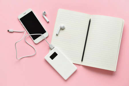 Modern power bank, mobile phone and earphones on pink background