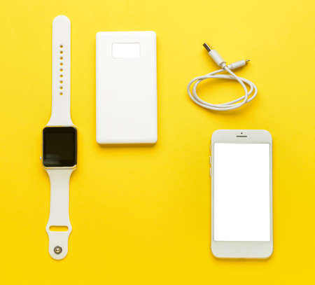 Modern power bank, smartwatch and mobile phone on yellow backgroundの写真素材