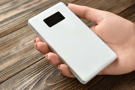 Woman holding modern power bank on wooden background