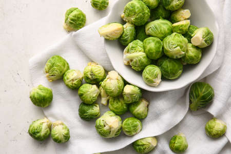 Bowl with fresh ripe Brussels cabbage on light background
