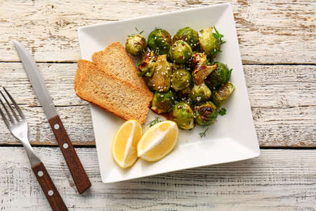 Plate with tasty roasted Brussels cabbage, toasts and lemon on light wooden backgroundの写真素材