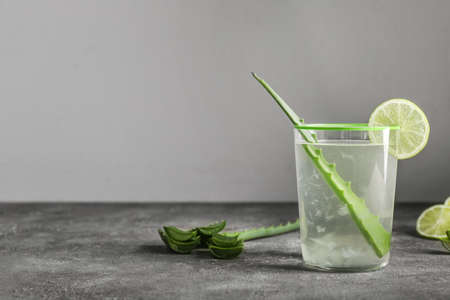Glass of aloe juice with leaf and lime on table against gray backgroundの写真素材